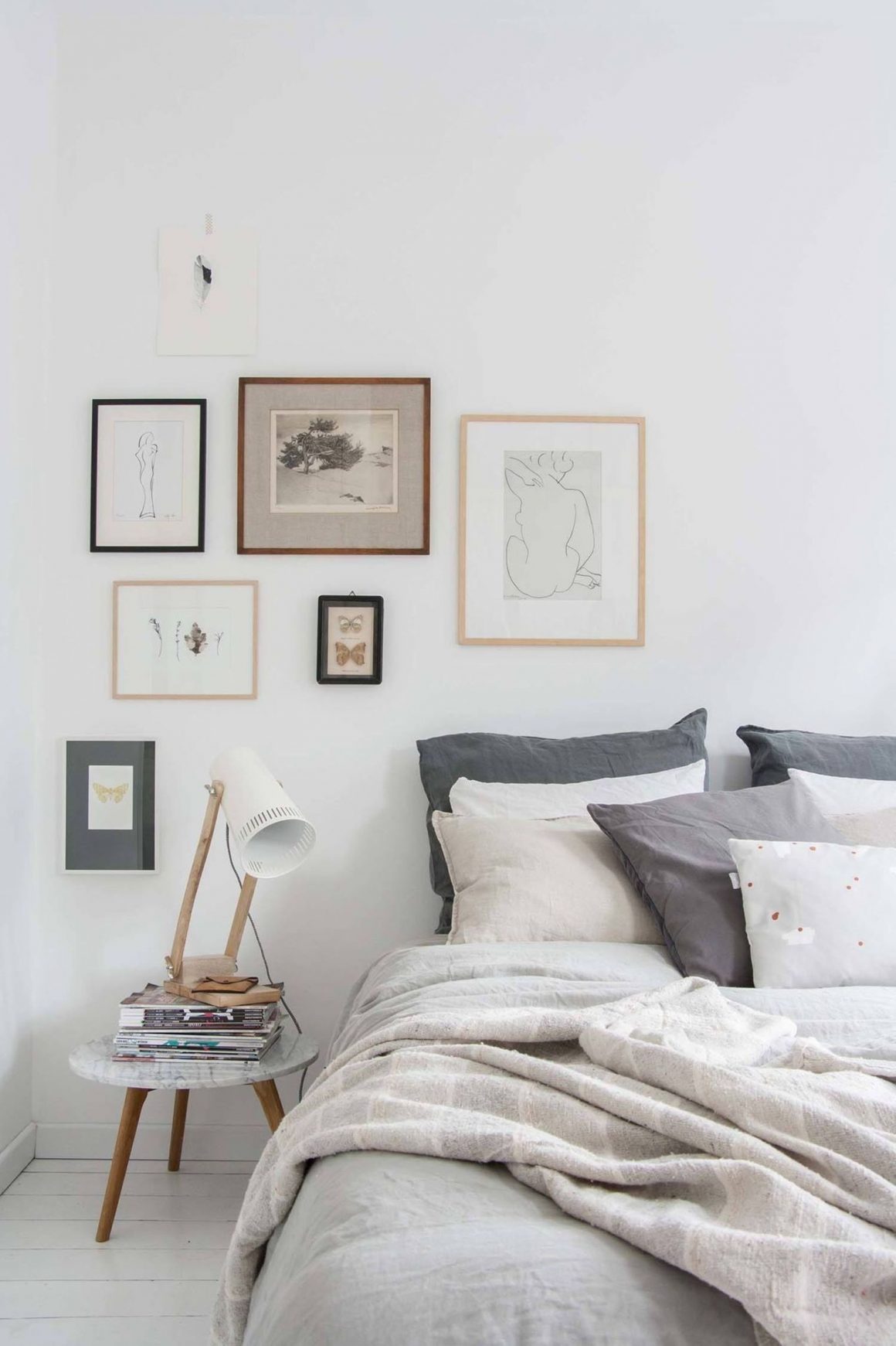 chambre avec draps de couleurs claires et cadres en bois sur mur blanc