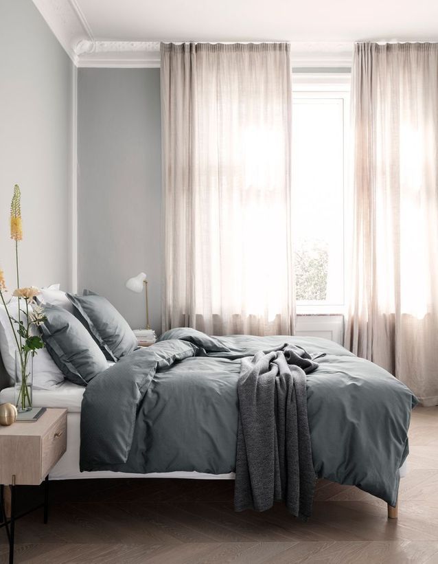 chambre lumineuse avec rideaux fins et draps gris sur le lit