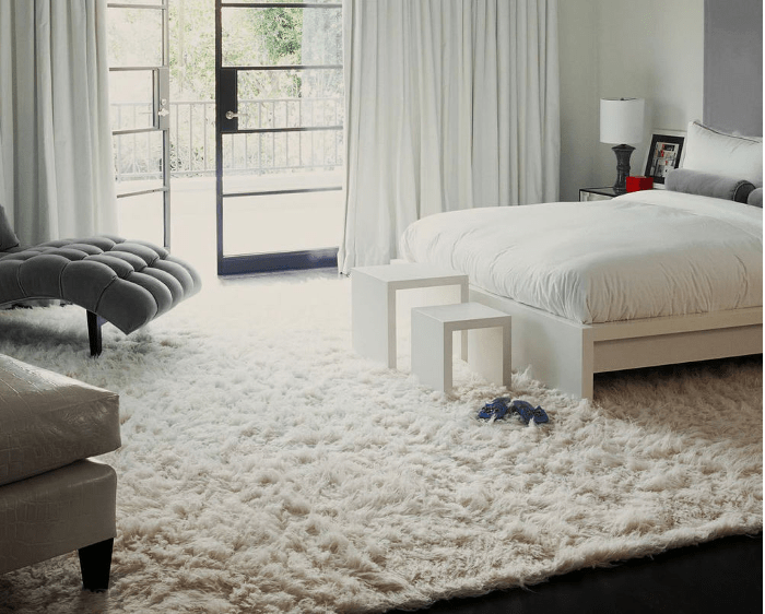 Grand tapis blanc à poils longs dans chambre adulte avec lit blanc et fourniture moderne