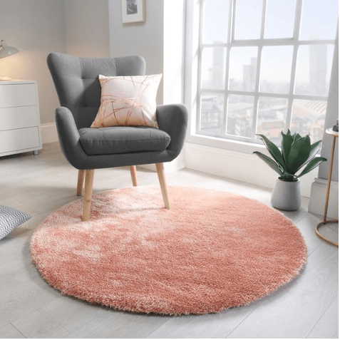 tapis shaggy rond de couleur rose sous un fauteuil scandinave gris