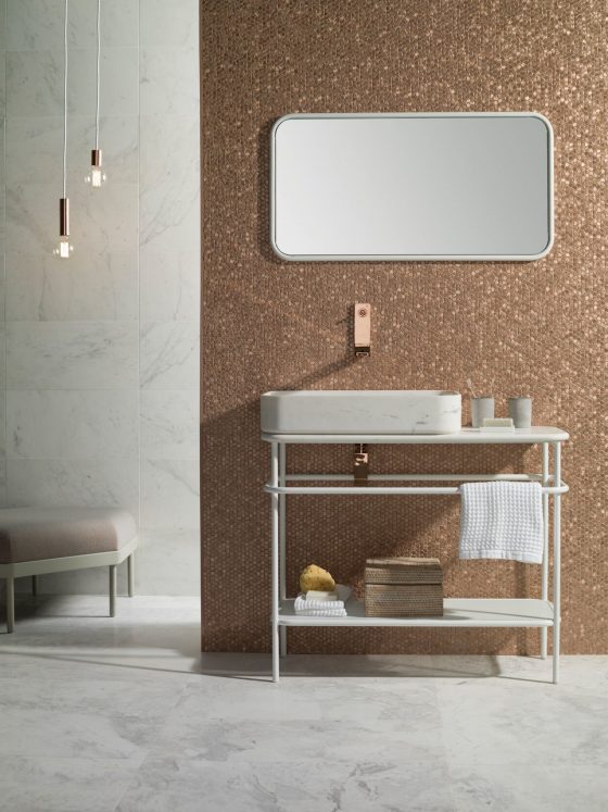 Une salle de bains au sol marbré et dont le mur est incrusté de mosaïque en rosé doré