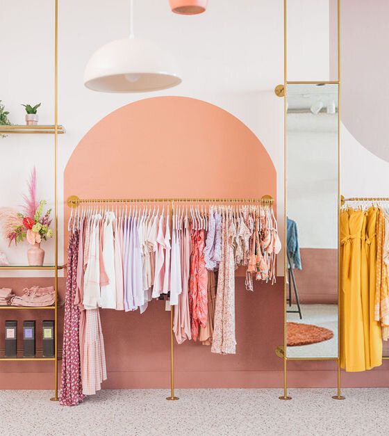 vêtements de couleurs sur portants en métal doré dans une boutique aux murs roses et saumon