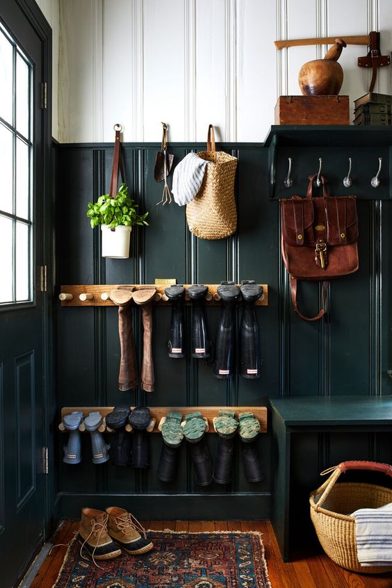 chaussures et sacs rangés contre le mur vert foncé de ce hall d'entrée