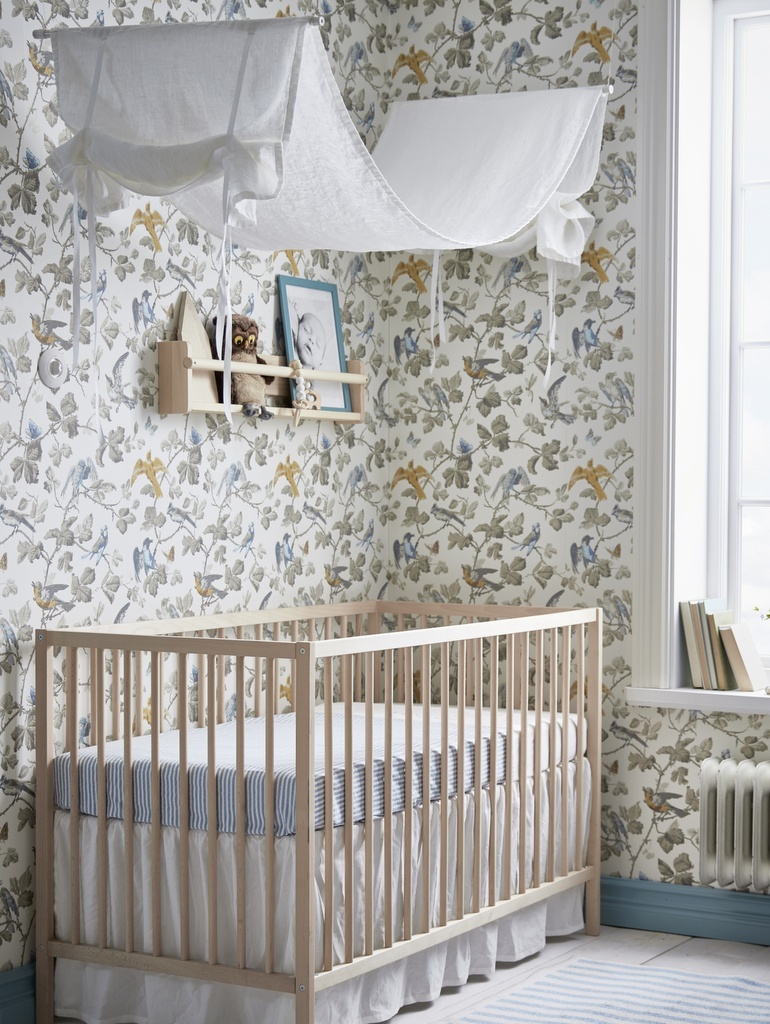 papier peint fleuri couvrant les murs autour d'un berceau en bois dans une chambre bébé