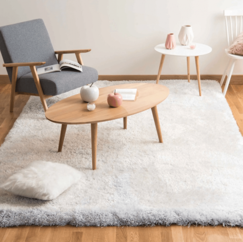 fauteuil rétro et table basse en bois de style scandinave sur un tapis à poils long de couleur gris clair