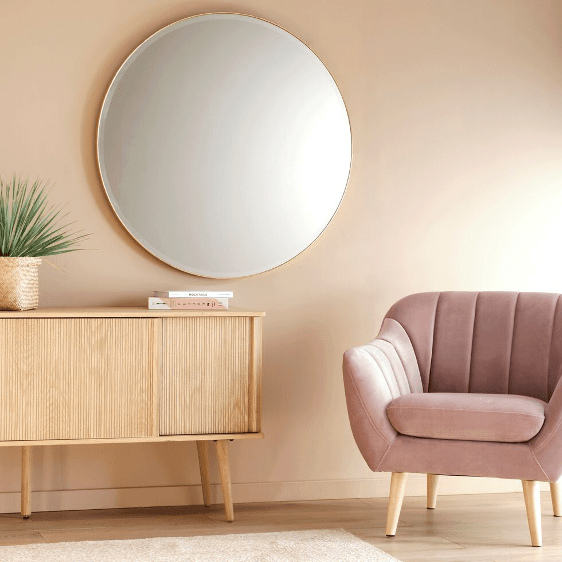 miroir rond accroché à un mur saumon a côté d'un fauteuil rose