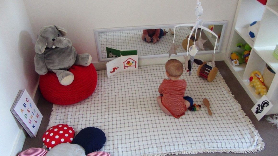 un bébé en tenue rouge sur une couverture au sol formant un nido avec miroir