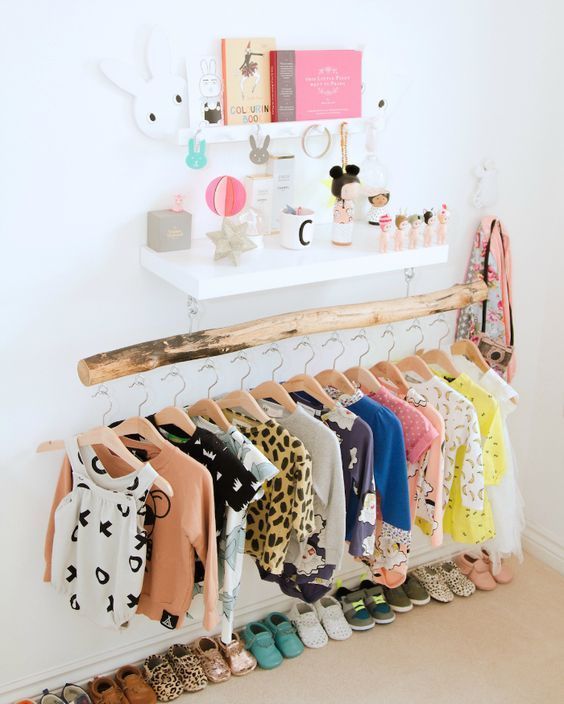 vêtements pour bébés sur un portant en tronc d'arbre sec dans une chambre bébé
