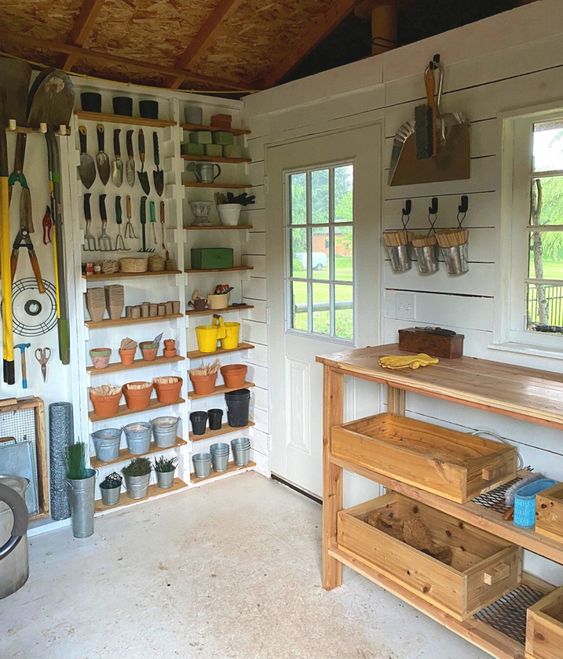 outils de jardinage rangés sur des étagères dans cabane de jardin blanche