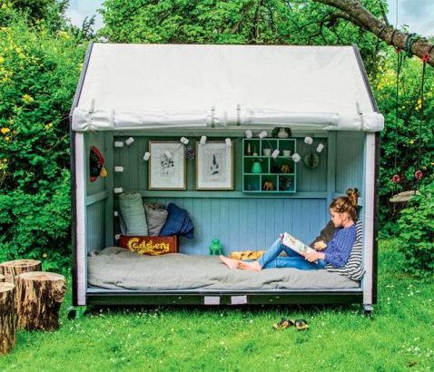 enfant lisant un livre dans cabane de jardin bleue aménagée en coin de lecture