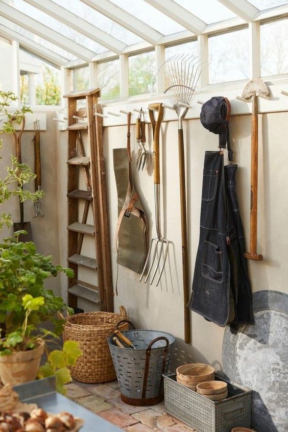 outils de jardinage accrochés au mur d'une cabane de jardin avec toit en verre