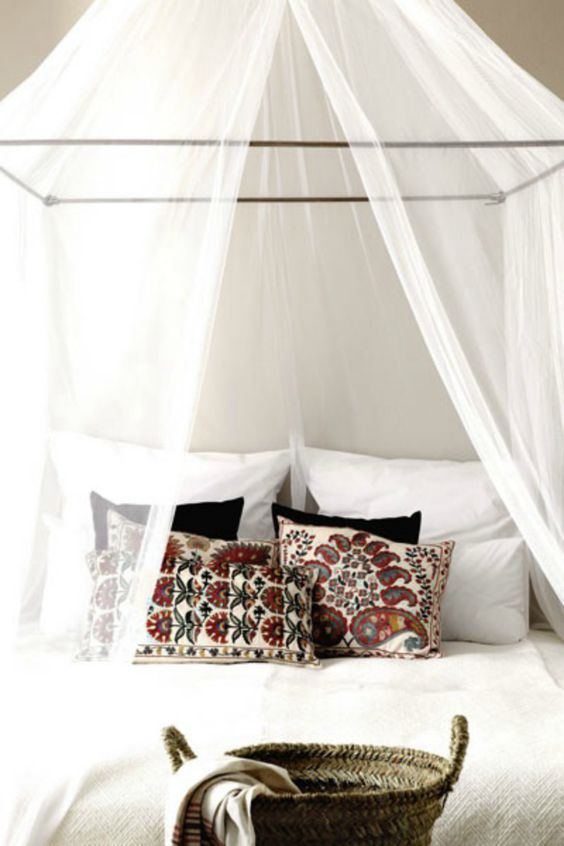 lit baldaquin avec moustiquaire blanche et des coussins colorés pour une déco été