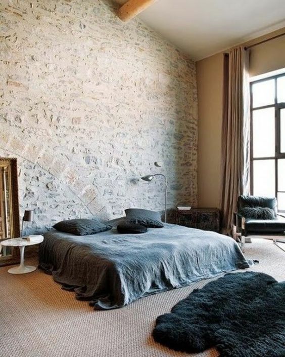 chambre à coucher contemporaine avec draps noirs et grand mur en pierre