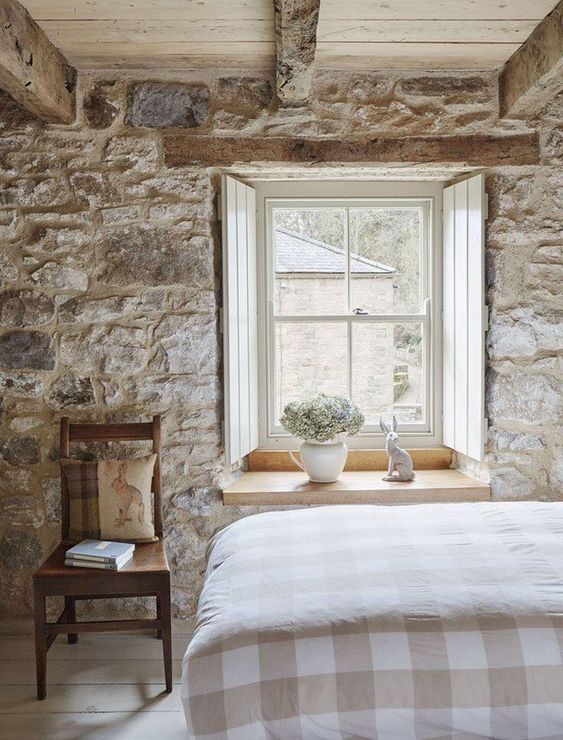 fenêtre en bois blanc dans une chambre à coucher en pierre et poutres apparentes
