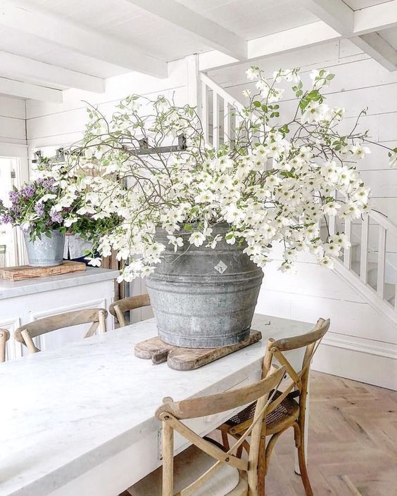 bouquet de fleurs blanches dans un vieil arrosoir disposé sur une table à manger rustique