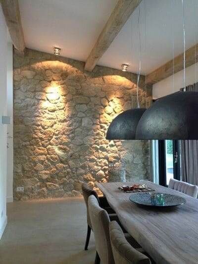 salle à manger au style classique avec grande suspensions et mur en pierre éclairé par des spots