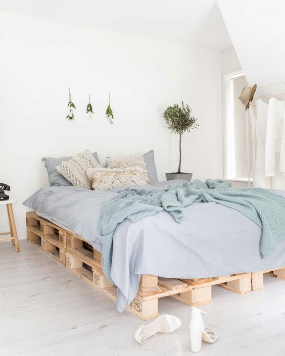 linge de lit en nuances de bleu sur un lit en palettes de bois clair dans une chambre lumineuse