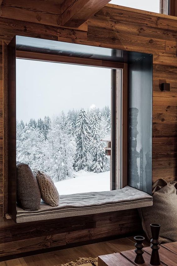 fenêtre dans chalet donnant sur une montagne enneigée