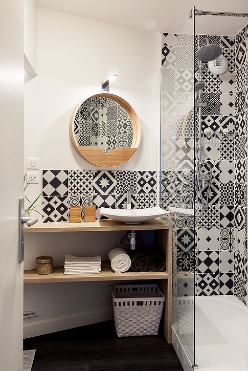 carreaux de faïence noirs et blancs à motifs géométriques dans douche et derrière vasque petite salle de bains