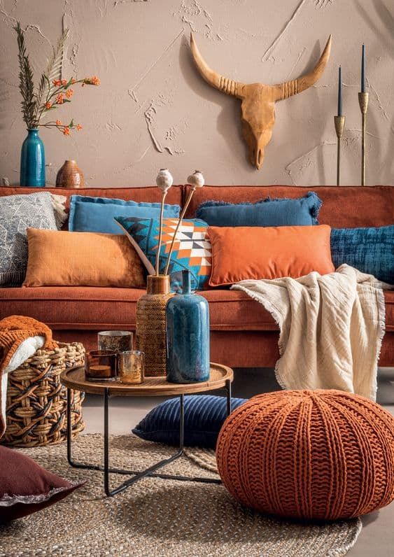 coussins oranges et bleus sur un canapé en velours orange dans une déco ethnique avec et pouf tissé