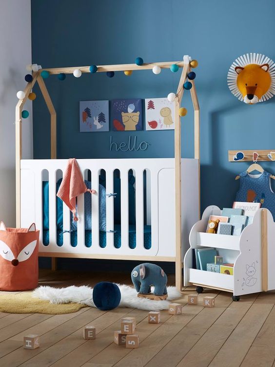 guirlande en boules de différentes couleurs autour des barreaux du lit d'une chambre bébé bleue au mobilier blanc