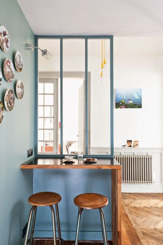 mini verrière de cuisine peinte en bleu derrière un bar en bois massif
