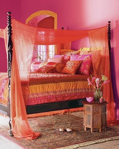 voilages rouges au dessus d'un lit à baldaquin garni de coussins bariolés à motifs graphiques dans une chambre au style oriental