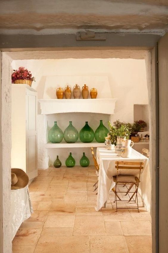 salle à manger déco méditerranéenne avec nappe blanche sur table à manger et jarres en verre soufflé sur des étagères en gypse