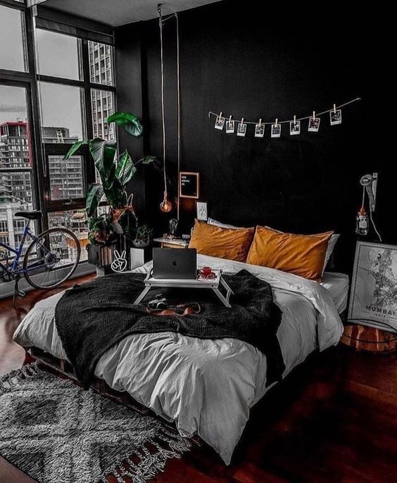chambre de style urbain avec mur noir et longues suspensions au dessus d'un lit avec draps gris et blancs