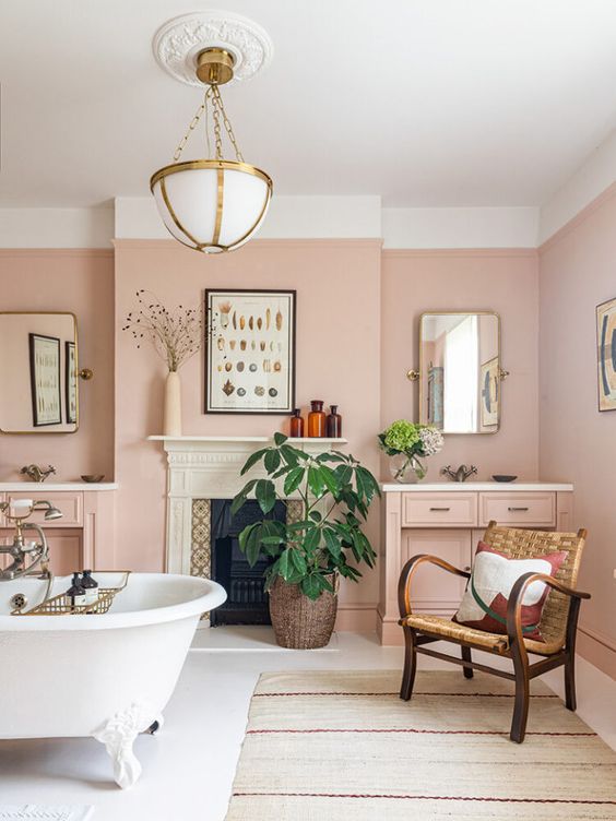 salle de bains rose déco romantique avec une baignoire en céramique et un fauteuil vintage en osier