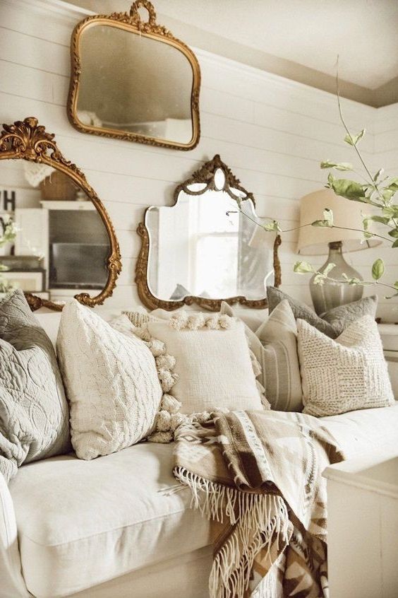 ambiance romantique dans un salon avec accumulations de coussins blancs sur un canapé cosy en lin en dessous de miroirs vintage dorés