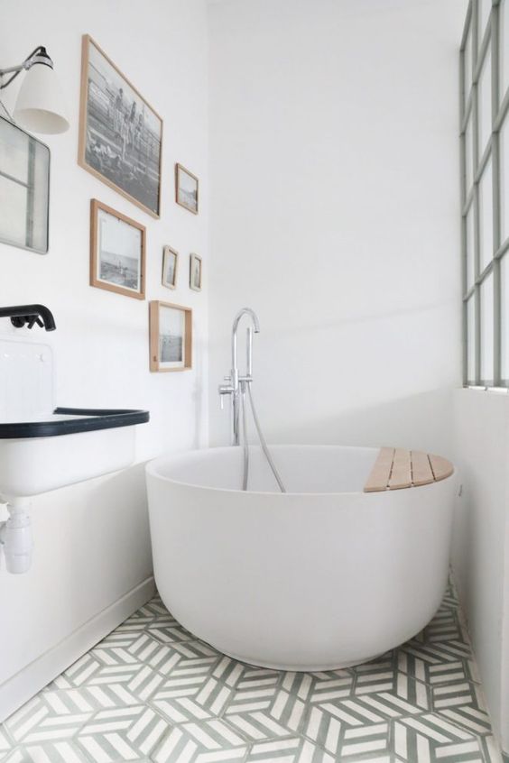 baignoire ronde en céramique dans une salle de bains blanche avec cadres vintages au mur