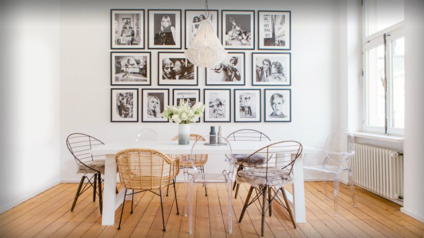 Un mur s'orne d'une dizaine de photos en noir et blanc, derrière une table et des chaises dépareillées