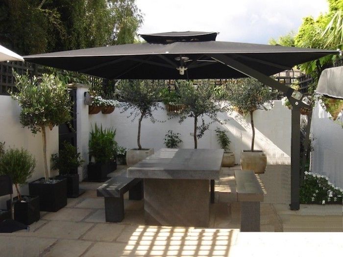 Un grand parasol gris déporté ombrage une table rectangulaire sur la terrasse