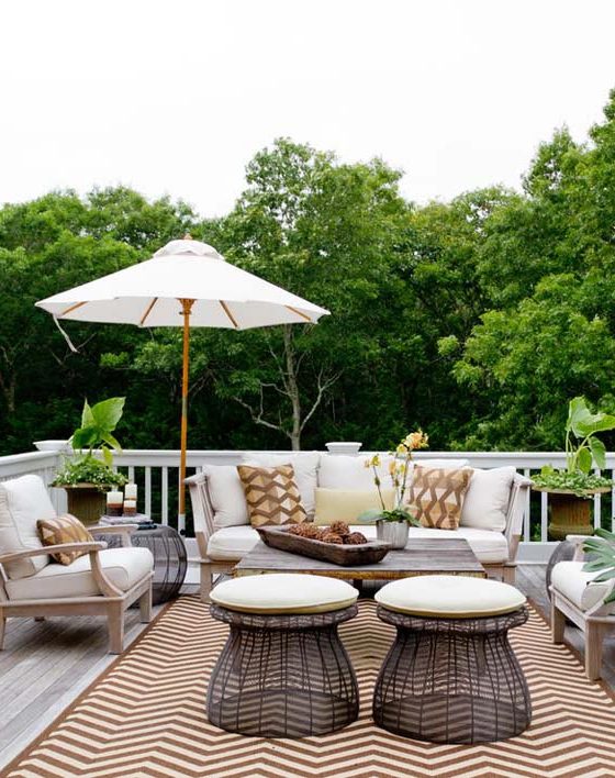 Une grande terrasse avec vue sur la nature, un tapis graphique et un salon de jardin en bois