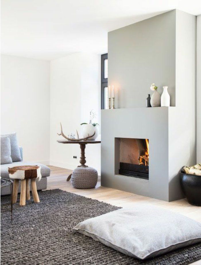 Une pièce de vie cocooning avec un aménagement cheminée simple et design : un tapis au sol et un pouf à côté du foyer