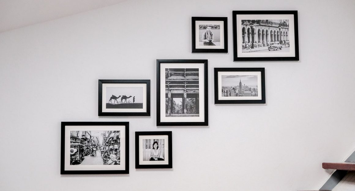 Plusieurs cadres noirs, avec des photos en noir et blanc, de différentes tailles, sont placés en diagonale sur le mur