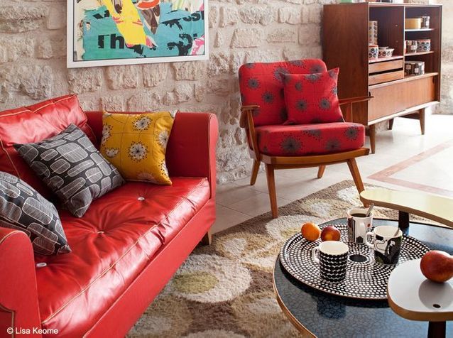 Un salon déco des années 50, avec un canapé rouge vif et des coussins aux motifs rétro