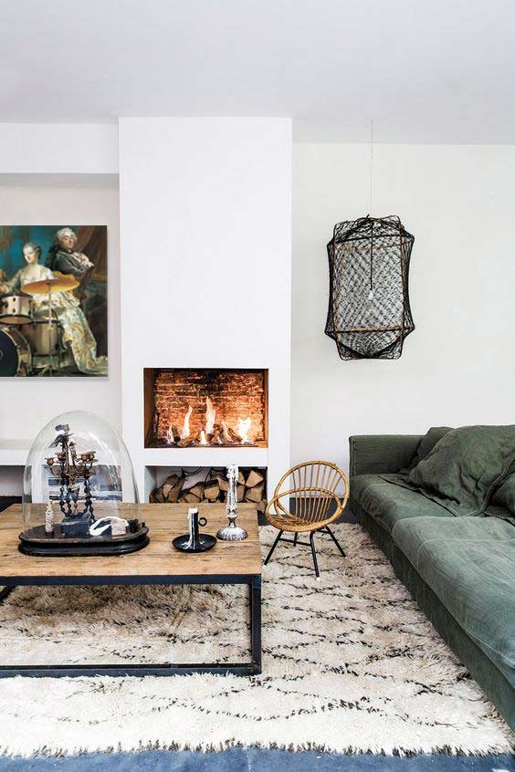 Cheminée blanche devant un tapis moelleux aux motifs géométriques, une table en bois et un canapé vert-gris