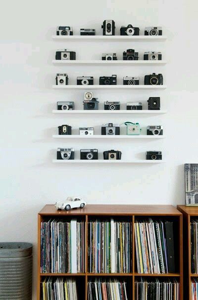 Une collection d'appareils photo disposés de manière soignée sur des étagères blanches