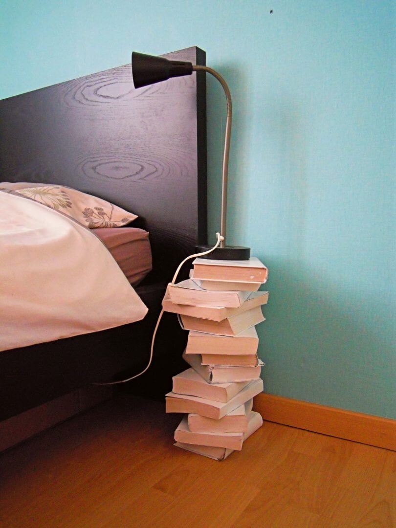 table de chevet diy confectionnée avec une piles de livres blancs, à côté d'une tête de lit foncée
