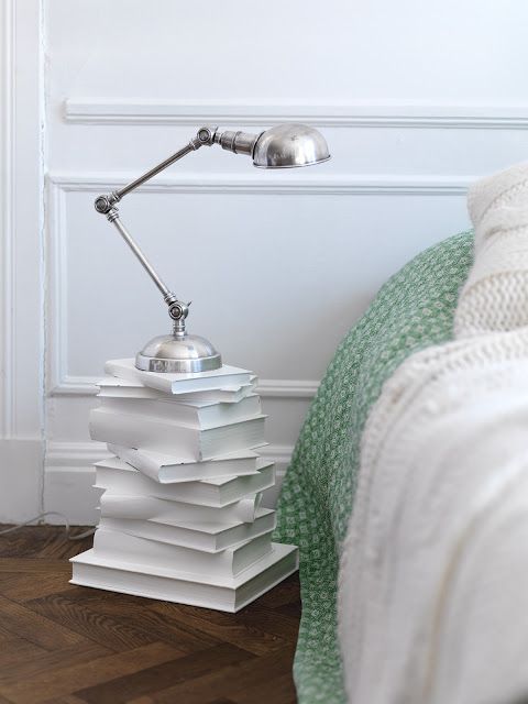 table de nuit faite avec une pile de livres blancs, surmontés d'une lampe de chevet
