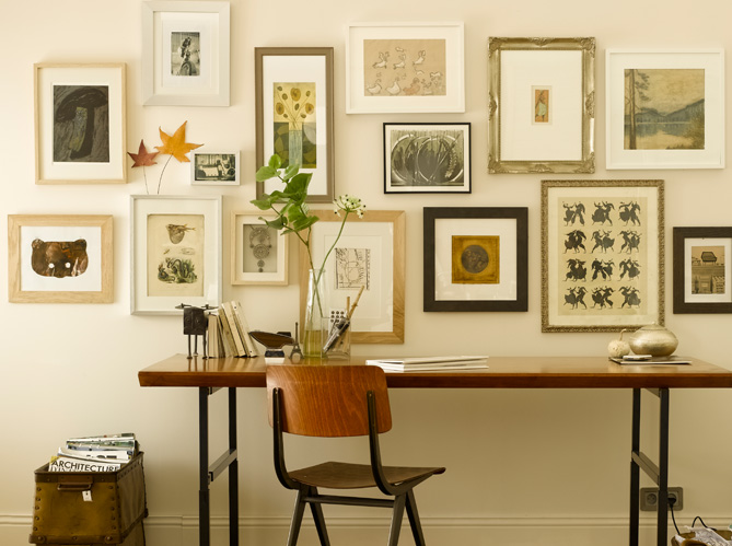 Un bureau face au mur, orné de cadres de toutes les tailles, représentant des végétaux ou des insectes