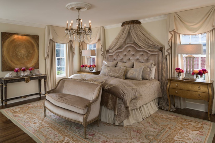 Grande chambre d'inspiration victorienne, avec un lustre, un tapis et un grand lit, dans les tons beiges