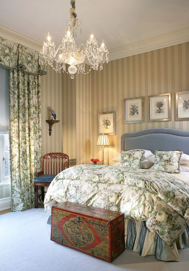 Chambre à la décoration victorienne, avec un grand lit aux draps fleuris, des rideaux et du papier peint à carreaux