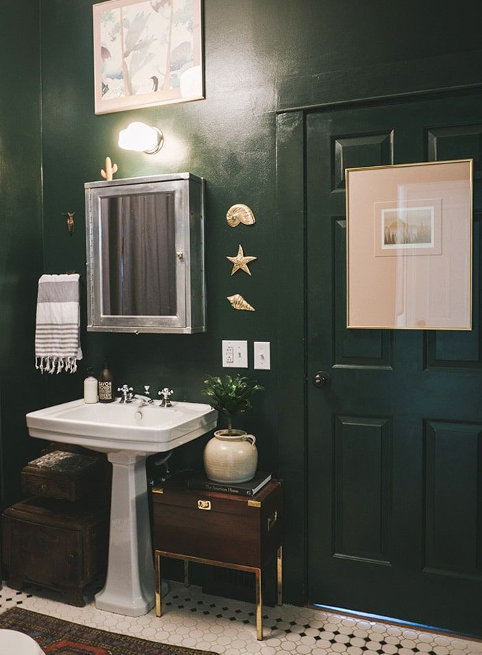 Une salle bains aux murs vert foncé, avec un lavabo en faïence blanc et un miroir accroché au-dessus