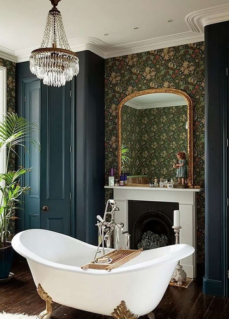 Une greande salle de bains à la décoration victorienne, avec une baignoire sur des pieds en forme de pattes de lion, une cheminée et du papier peint fleuri