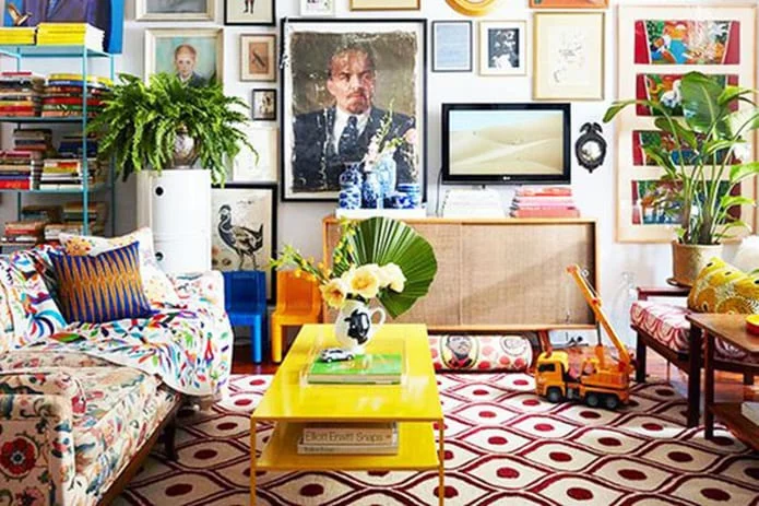 Un salon maximaliste avec un tapis à motifs géométriques, une table basse jaune et un canapé fleuri