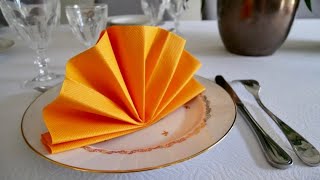 Une serviette orange pliée en forme de queue de paon, pour compléter la décoration de table jour de l'an