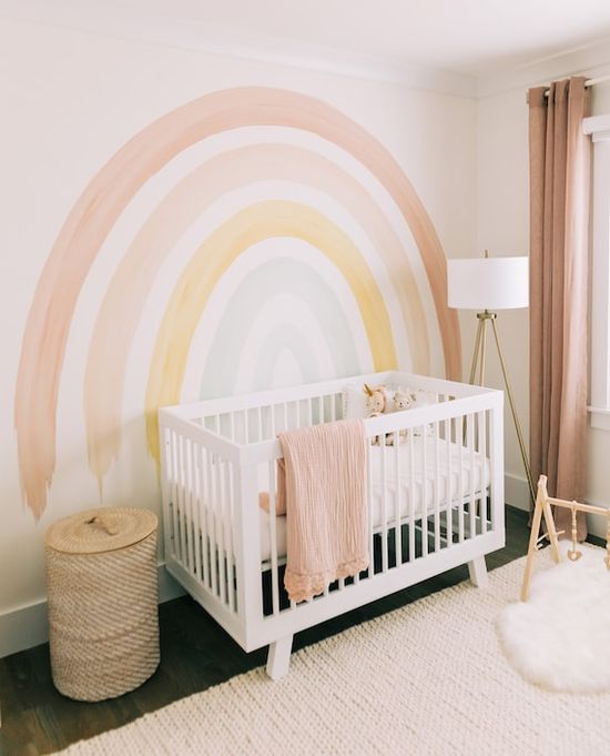Une chambre de nouveau-né décorée avec des tons pastel, un arc-en-ciel au mur et un lit blanc